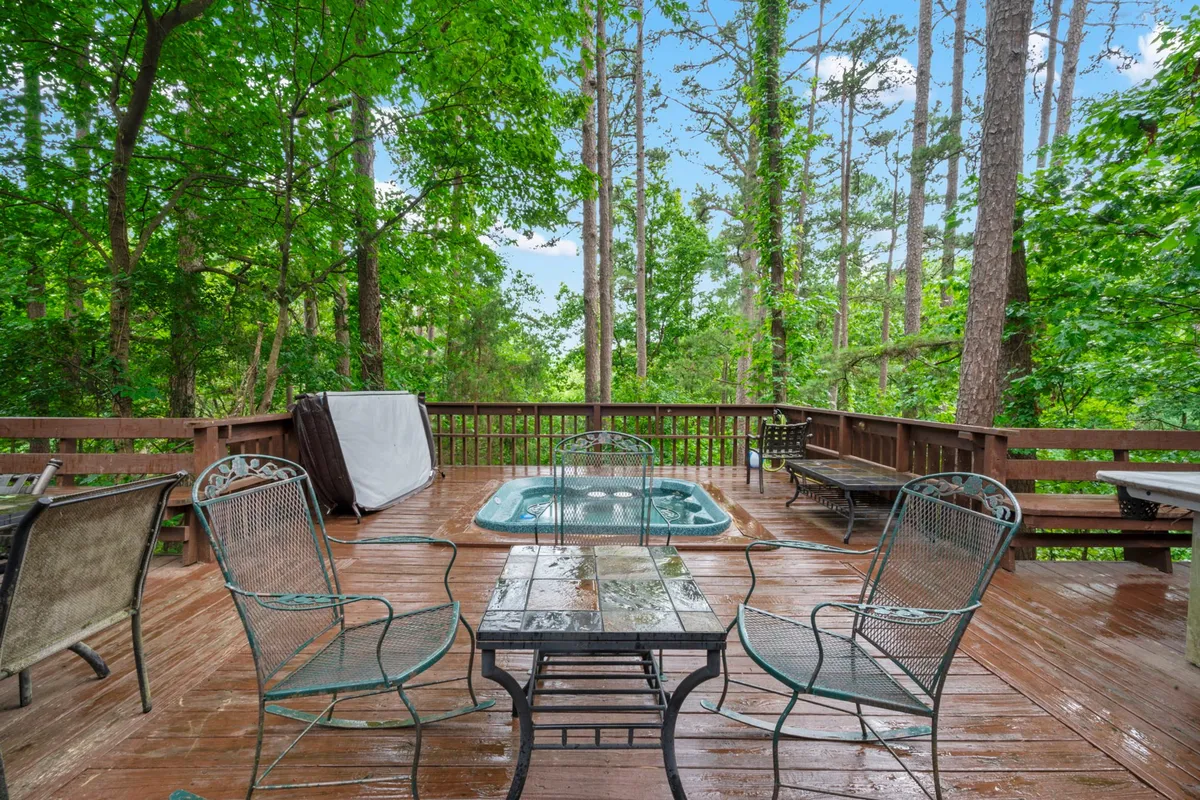 An inviting outdoor deck area with a hot tub nestled among tall pines. Comfortable seating surrounds the space, offering a peaceful spot to relax and soak up the tranquil forest views.