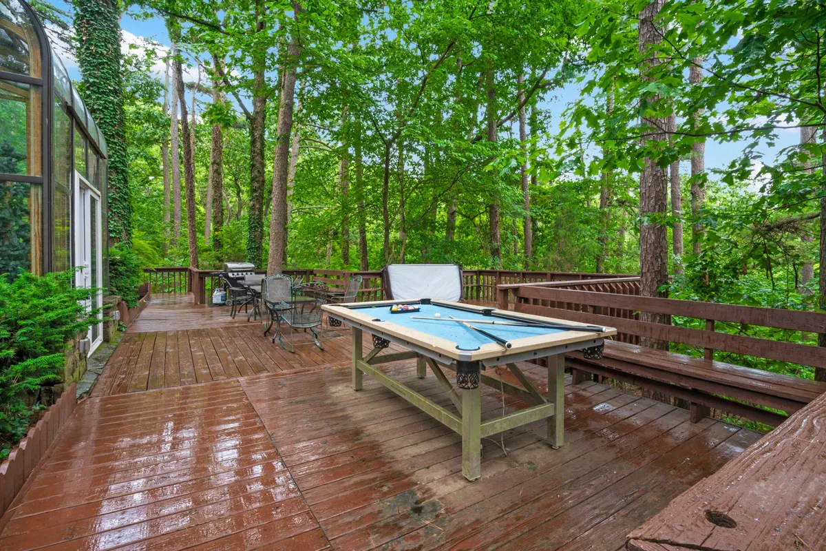 An outdoor wooden deck featuring a pool table, bordered by trees. The area offers a casual, social environment for friendly competitions and relaxation amidst nature.