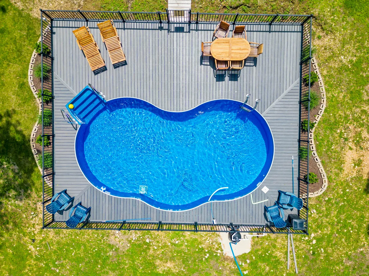 An inviting swimming pool is surrounded by an outdoor dining table and lounge chairs, set against a backdrop of lush greenery. The space is designed for group gatherings, sunbathing, and enjoying relaxed meals outdoors.