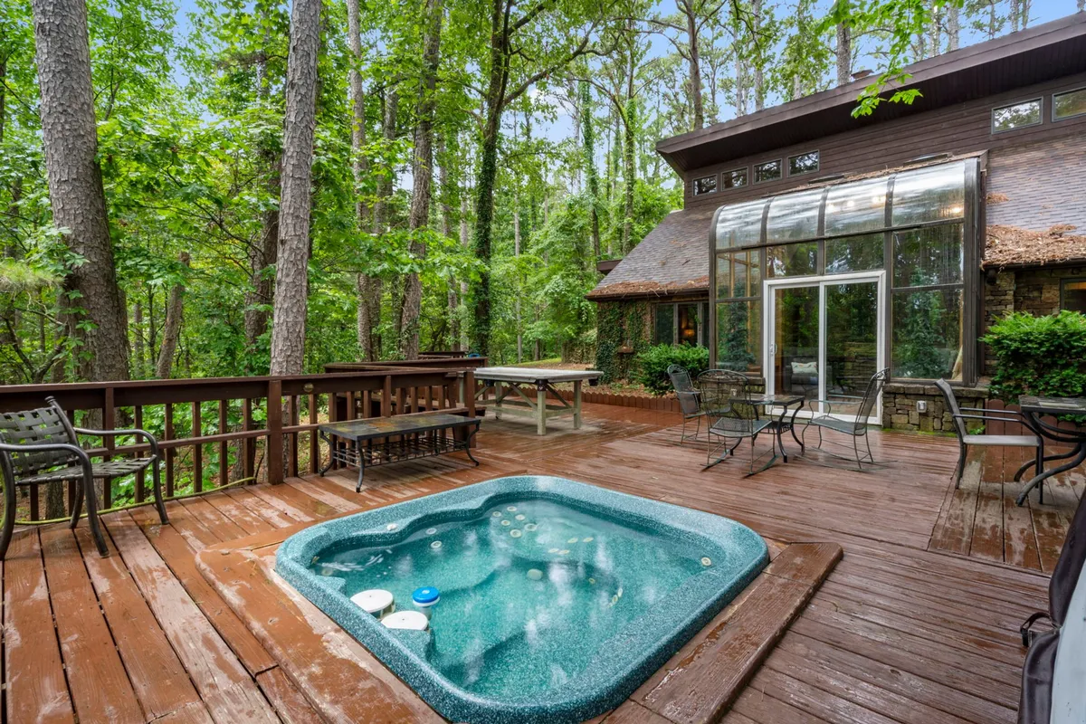 A serene hot tub sits on a wooden deck, partially enclosed by a glass wall with views of surrounding trees. The space invites relaxation, stargazing, and group gatherings in a peaceful outdoor atmosphere.