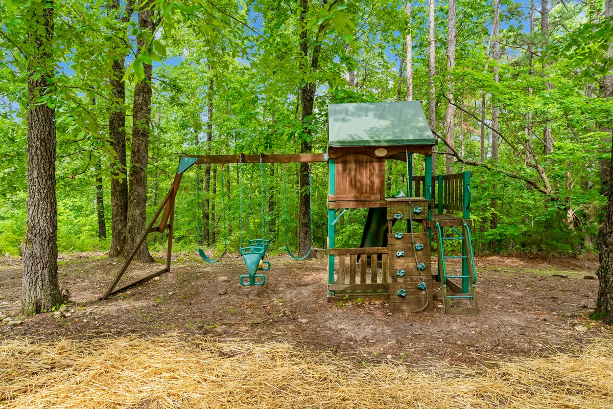 An engaging playset with a swing and climbing wall sits in a grassy area surrounded by trees, inviting children to explore and families to spend time together outdoors.