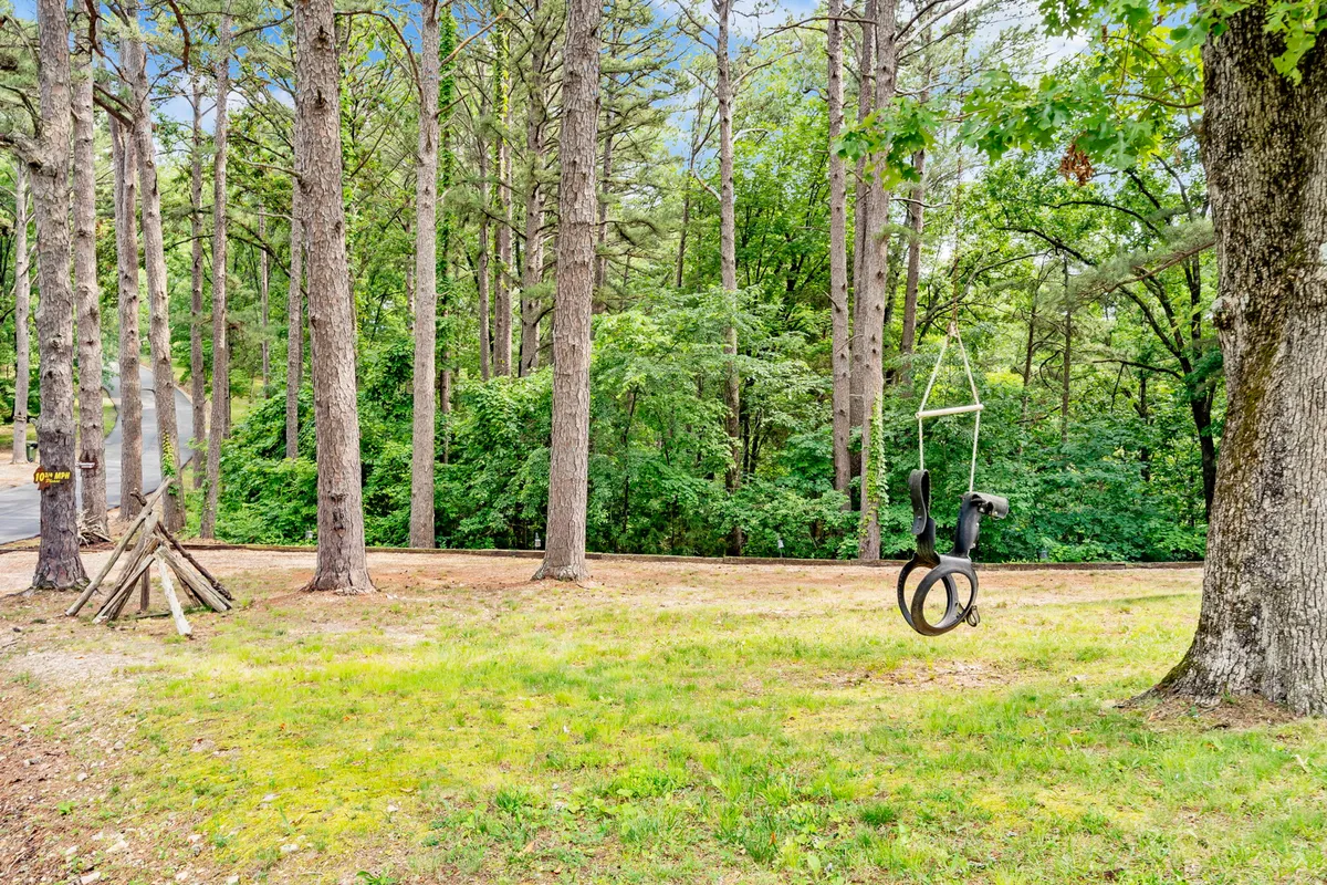 A playful swing set nestled in a grassy area, beneath tall trees. There is ample space for kids to play and families to picnic or enjoy outdoor games together, surrounded by nature.