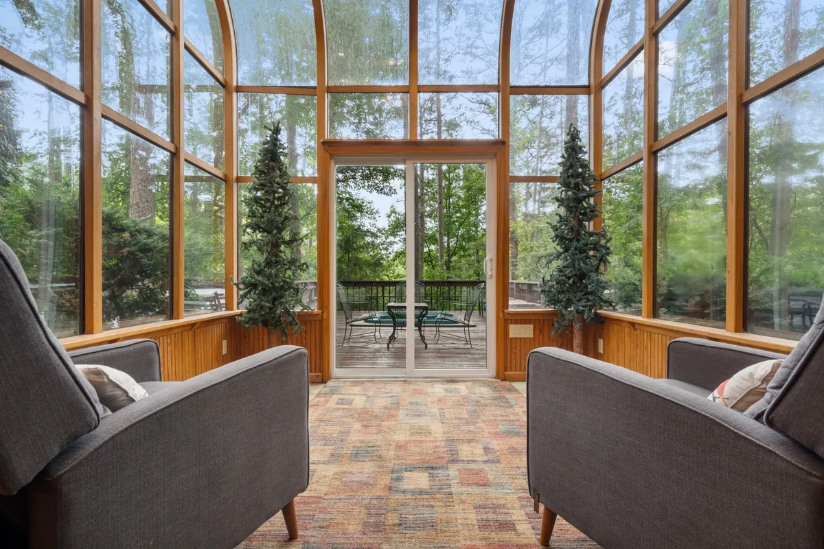 A striking solarium with two grey armchairs positioned by floor-to-ceiling glass walls that look out onto a lush forest. The space feels serene and immersive, offering a true sense of being inside the forest canopy while remaining sheltered and comfortable.